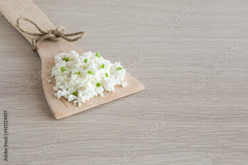 Cottage cheese in the wooden spoon with spring green onions on the table in the kitchen. Dairy product. Meal tasting. Healthy eating and lifestyle. © fotoduets