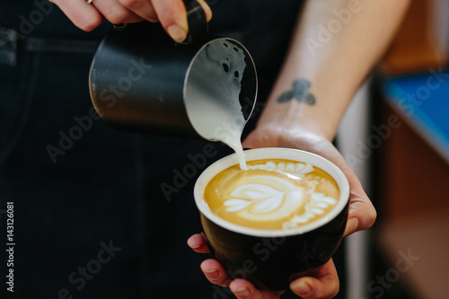 Close up of female barista's hands making coffee latte or cappuccino art in coffee shop.