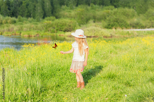 Little girl in a hat on a summer day playing with a butterfly in a field in the village © viclin