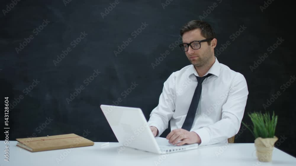 Portrait smiling businessman using laptop on blank chalkboard background Portrait smiling businessman using laptop on blank chalkboard background