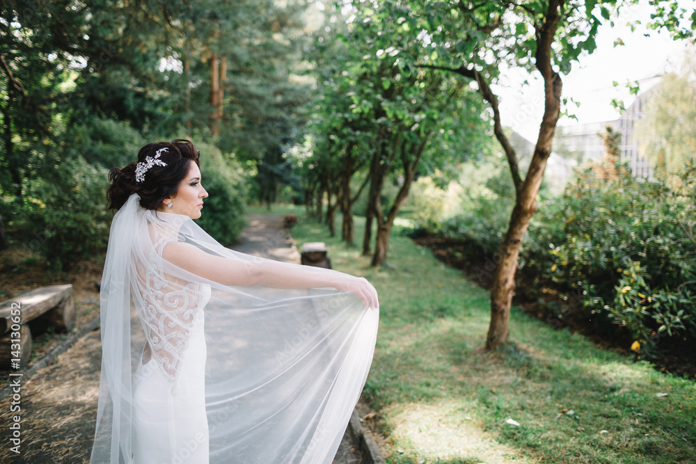 Bride whirls her veil walking along the path in park