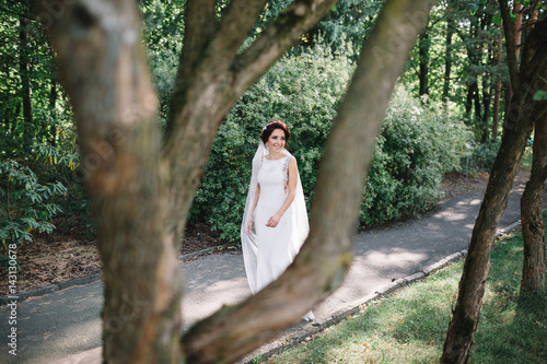 Look from behind a tree at pretty brunette bride in elegant gown