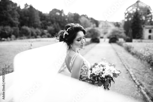 Wind blows bride's veil while she stands calmly in the park