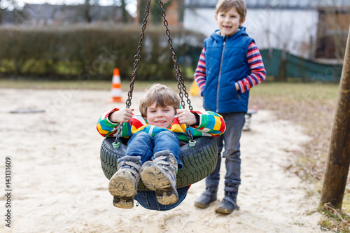 Two little kid boys having fun with chain swing on outdoor playground