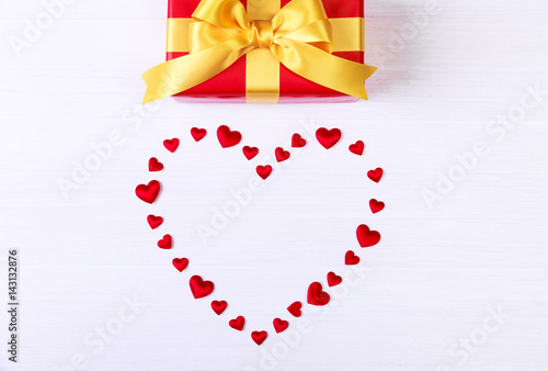 Gift box with red heart. Present wrapped with yellow ribbon. Christmas or birthday package. On white wooden table.