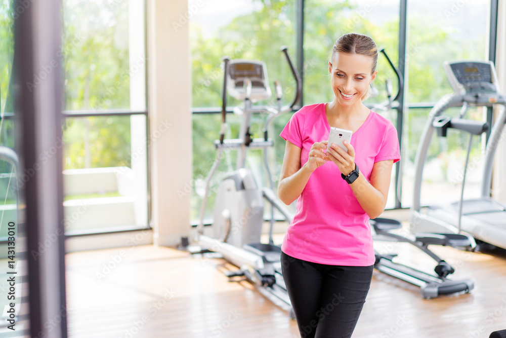 Fototapeta premium Sport lifestyle and technology. Attractive young woman using smartphone in gym.