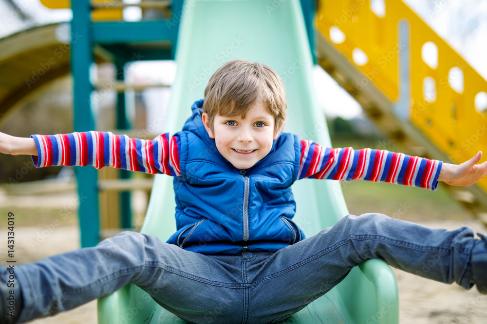 Happy blond kid boy having fun and sliding on outdoor playground Happy blond kid boy having fun and sliding on outdoor playground