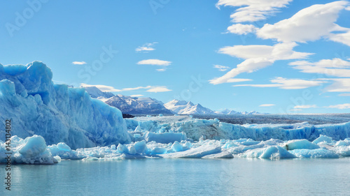 Single blue icebergs and blue sky with white clouds and mountains on the background. Upsala Glacier at Argentino Lake, Los Glaciares National Park, Patagonia, Argentina photo