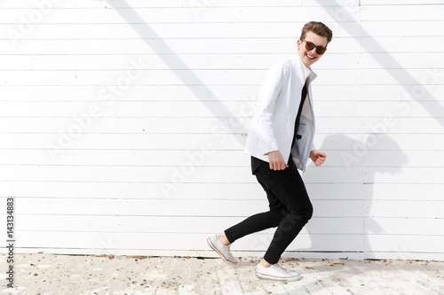 Cheerful man in sunglasses running over white wall background