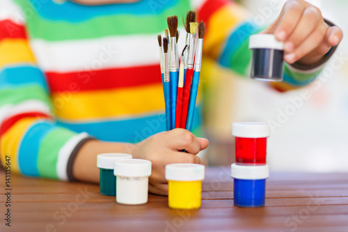 Close-up of hands of kid holding watercolors and brushes.