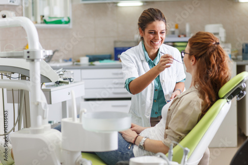 A professional female dentist  equipped with a bright smile  converses with her red hair female patient  carefully explaining the upcoming treatment  and ensuring her comfort throughout the process.