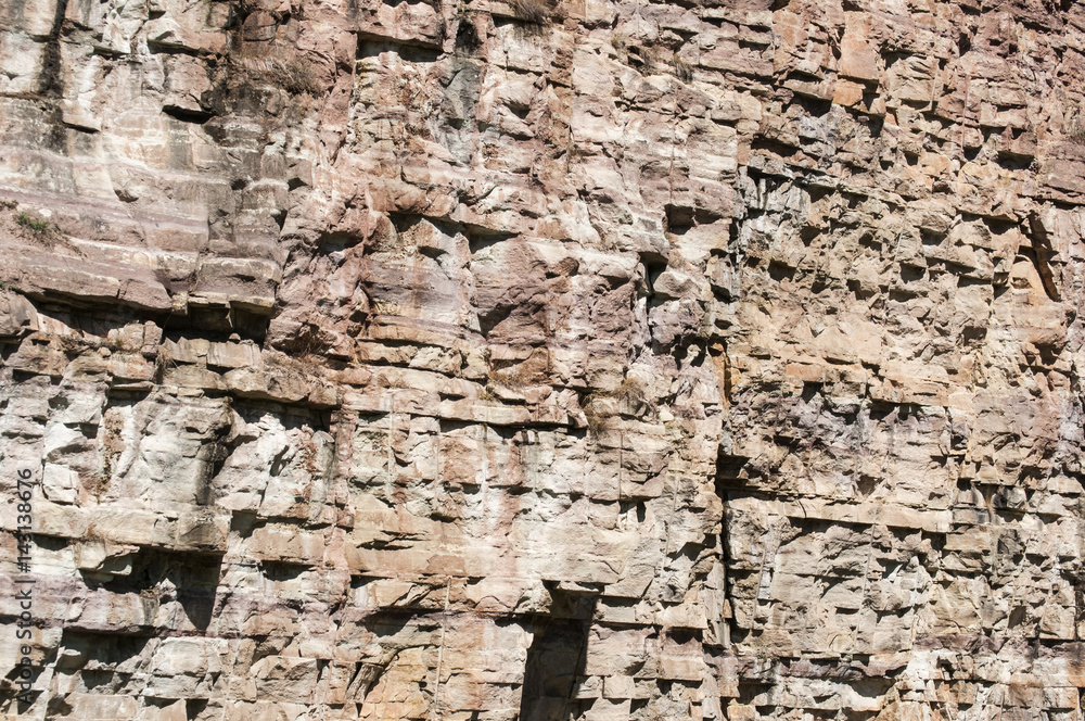 Fototapeta premium Vertical reddish wall of abandoned stone quarry closeup as natural background