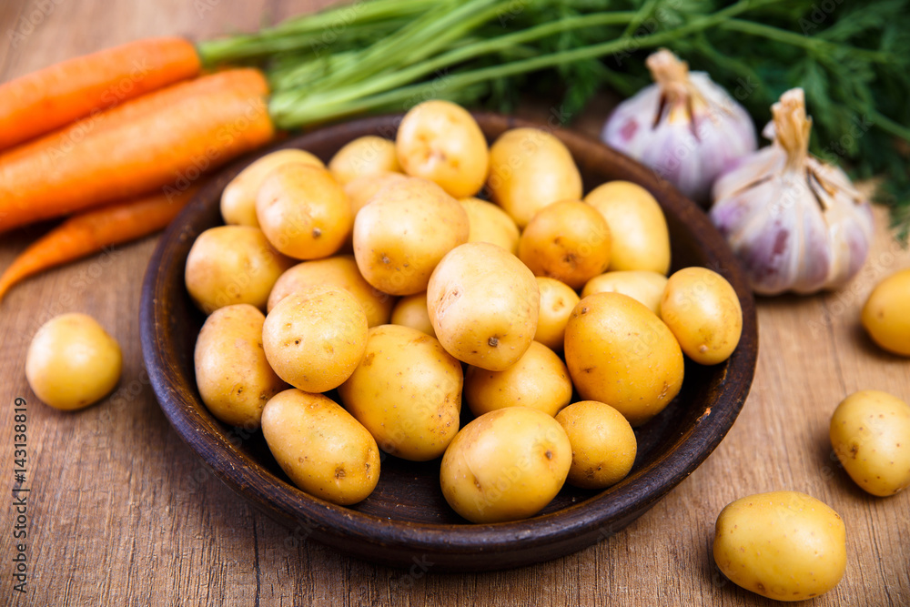Potatoes in plate. Carrot, garlic and raw new potato. Fresh natural vegetables. Organic bio food on rustic wooden table. Potatoes in plate. Carrot, garlic and raw new potato. Fresh natural vegetables. Organic bio food on rustic wooden table.