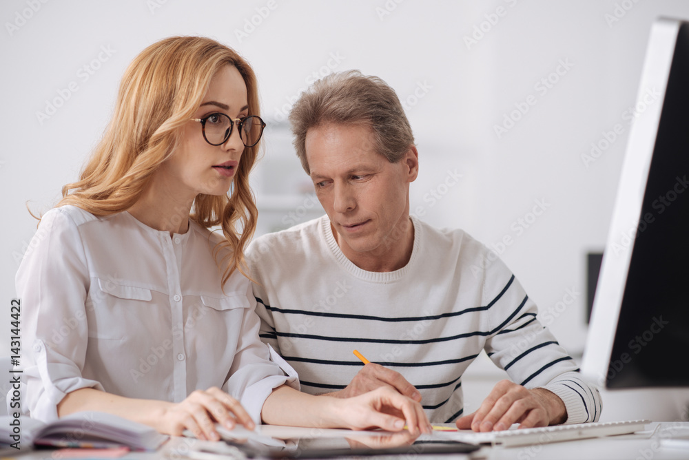 Aged office manager staring at young colleague at workplace Aged office manager staring at young colleague at workplace