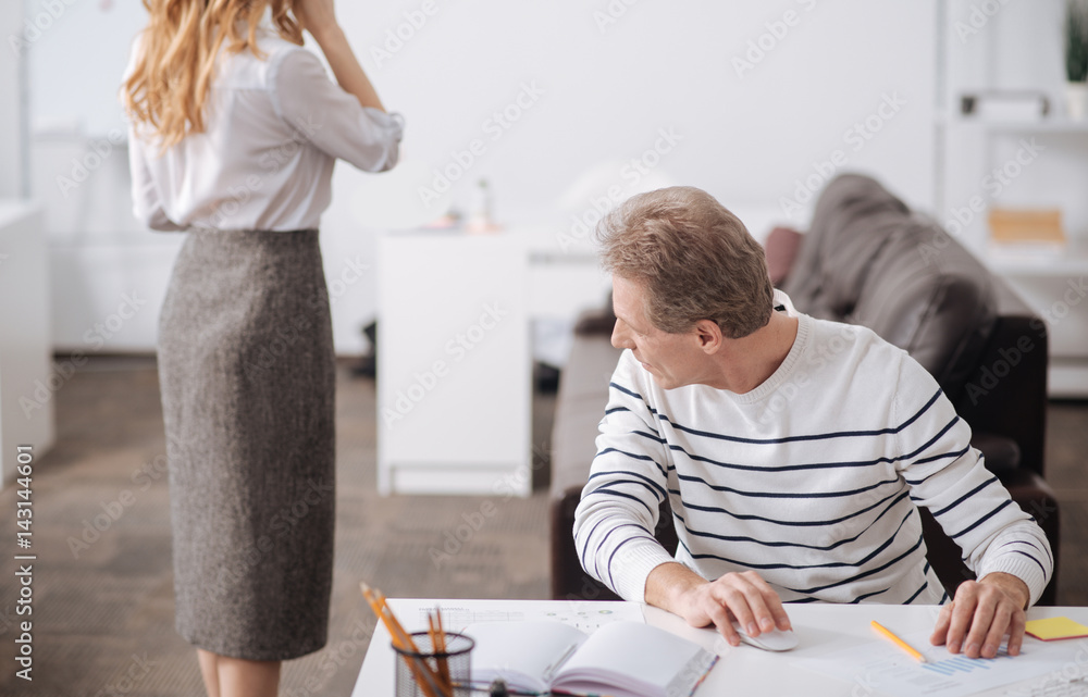 Fototapeta premium Playful aged businessman looking at young colleague body at work