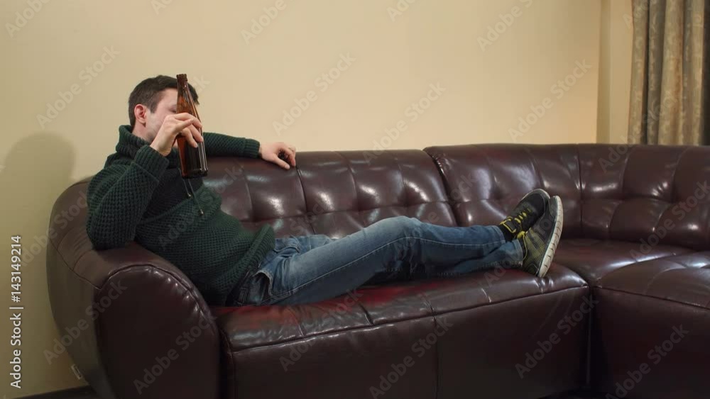 Young man is lying on the couch watching TV and drinking beer. Young man is lying on the couch watching TV and drinking beer.