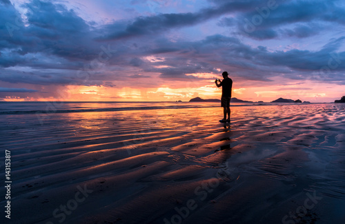 Silhouette, man taking a picture with a smartphone on the beach and wonderful sky at sunset. Andaman seaThailand