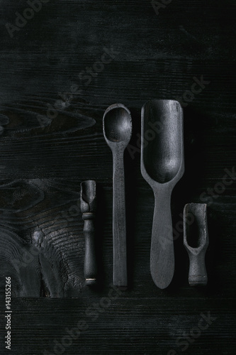 Black burnt wooden empty kitchenware cutting board, plates, scoop and spoon over black wood background. Flat lay with space