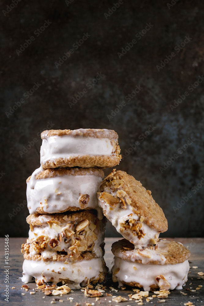 Set of homemade ice cream sandwiches in oat cookies with almond sugar crumbs over dark metal texture background. Close up