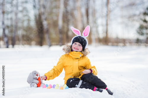 Cute girl with rabbit and baskets sitting in snow for walk.