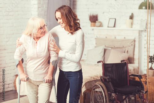 Photos Merry young woman helping disabled old lady at home