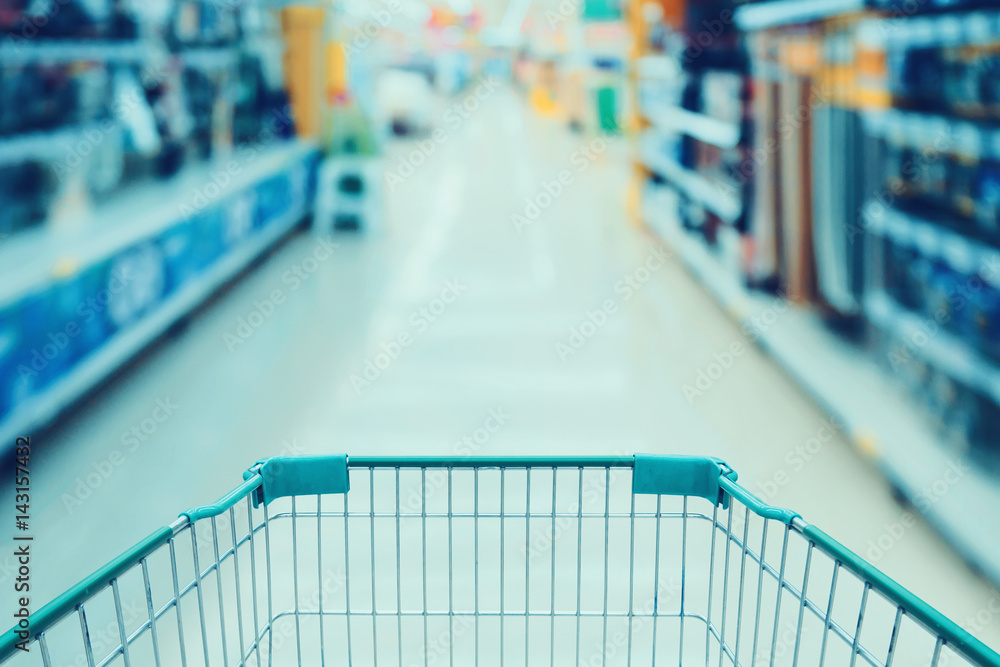 Supermarket aisle with empty green shopping cart blurred background Supermarket aisle with empty green shopping cart blurred background