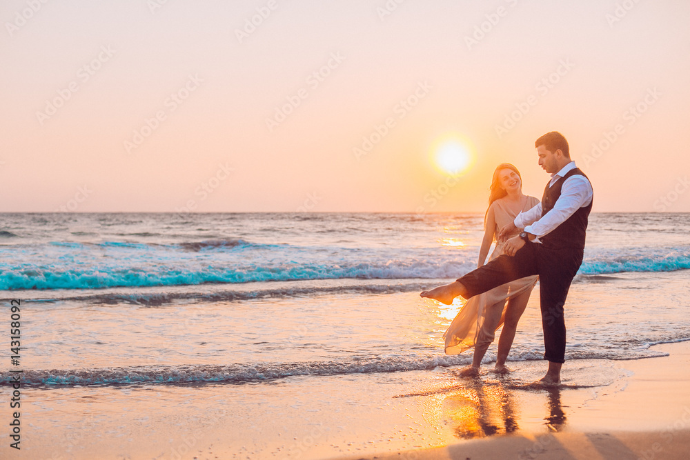 Honeymoon couple romantic in love at beach sunset. Newlywed happy young couple holding hands enjoying ocean sunset during travel holidays vacation getaway.