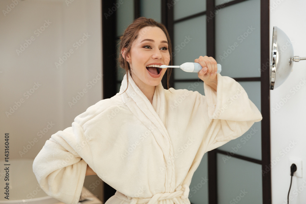 Happy young woman standing and brushing her teeth in bathroom Happy young woman standing and brushing her teeth in bathroom