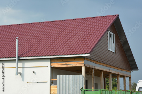 Roofing Construction with red metal roof tiles and metal chimney outdoors.