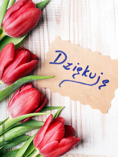 "Thank you" card (Polish word "dziękuję") and tulip bouquet on white wooden background