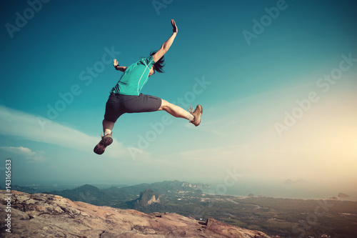 successful woman jumping on rocky mountain peak, freedom, risk, challenge, success concept