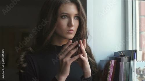 Beautiful young girl standing next to the window and drinking coffe.