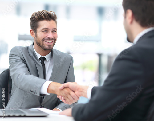 Two business people shaking hands and looking at each other with