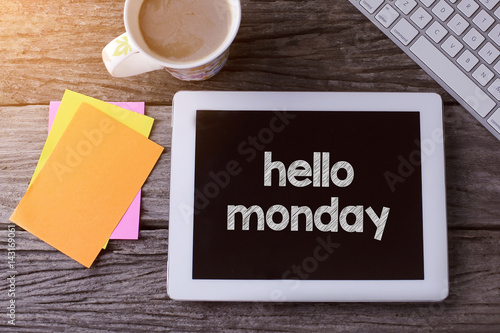 Tablet pc with hello monday and a cup of coffee on wooden background.