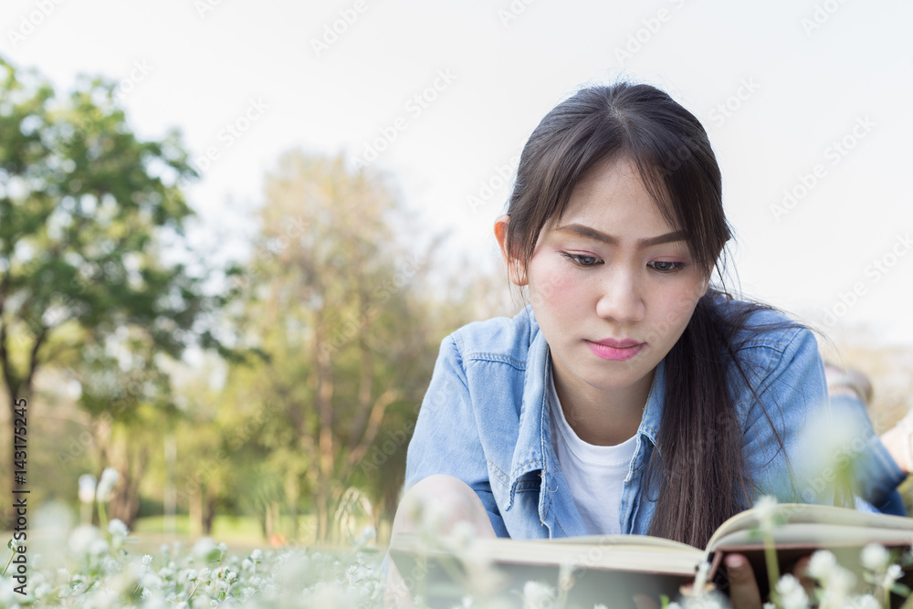 Young asian girl lying on flower field and reading books Young asian girl lying on flower field and reading books