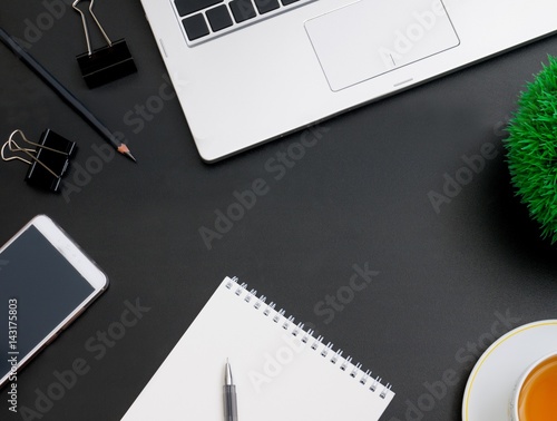 Modern dark office desktop computer, a mobile phone with a black screen on a laptop, and a Cup of tea. Top view with copy space, flat lay.