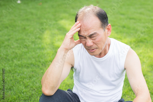 Asian old man headache and sitting in the grass , man stress and headache concept.