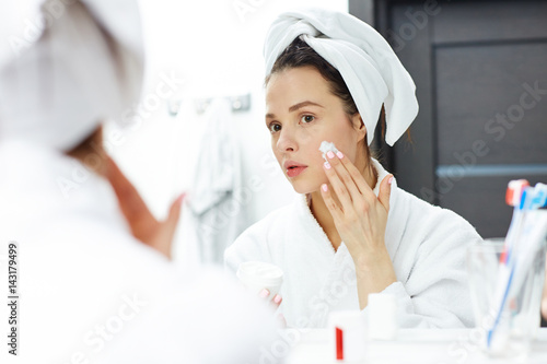 Fresh young woman applying cream on her face
