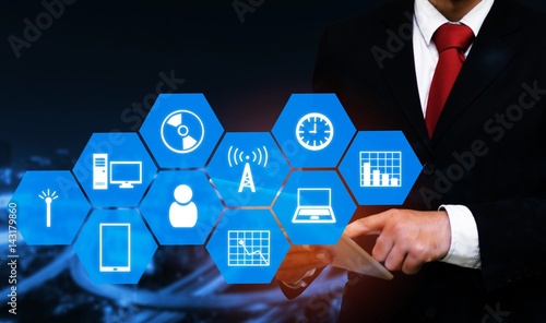 smart businessman in suit using his tablet with technology device icon and hexagon shaped pattern background, business and technology concept on blurred night city background, color tone effect.