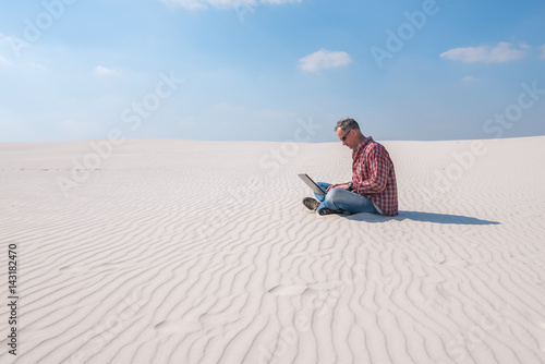 Man is passionate about work, with a laptop sits in desert