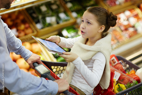 Dissatisfied girl with touchpad talking to her father in supermarket