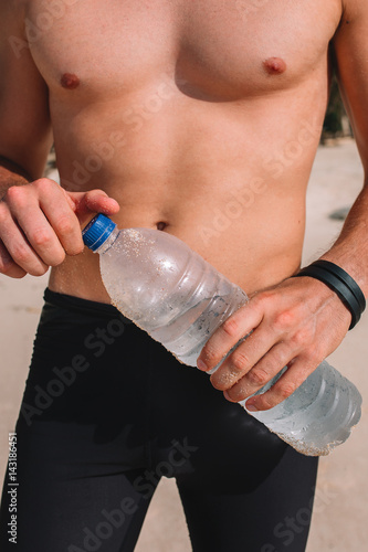 Sportsman is holding the bottle of water, close up. On the beach, Bali, Indonesia