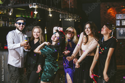 Young cheerful company of friends in the club bar having fun with multi-colored confetti and crackers celebrate