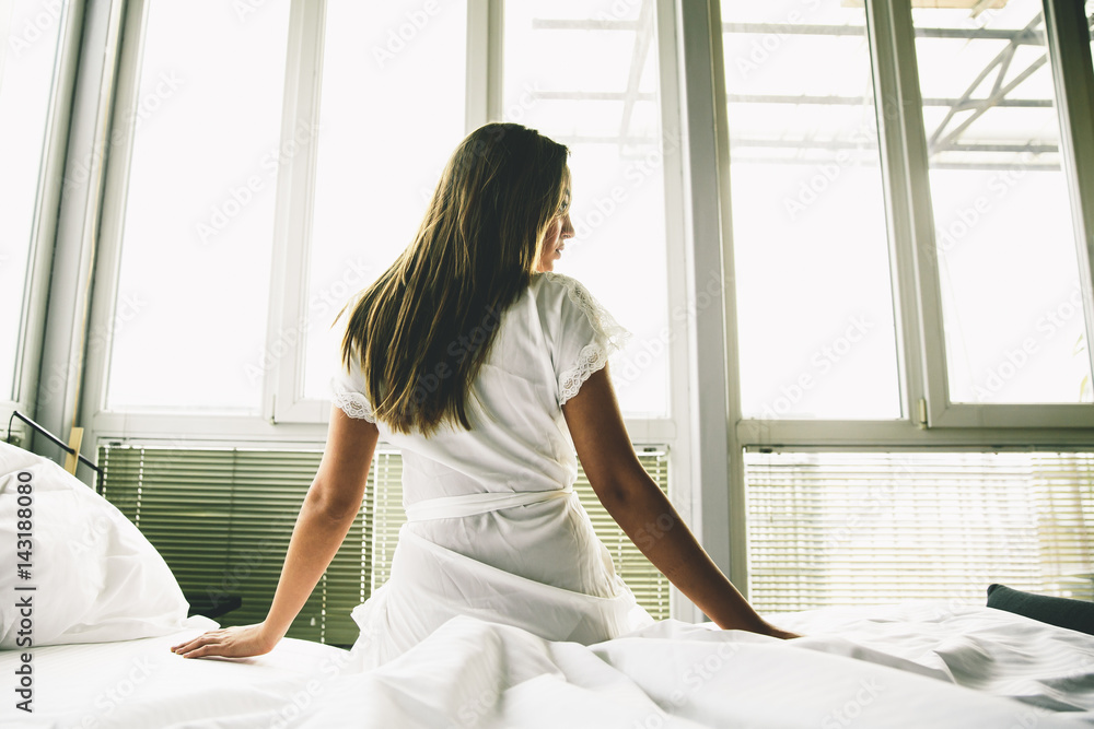 Young woman sits on a bed with white linen Young woman sits on a bed with white linen