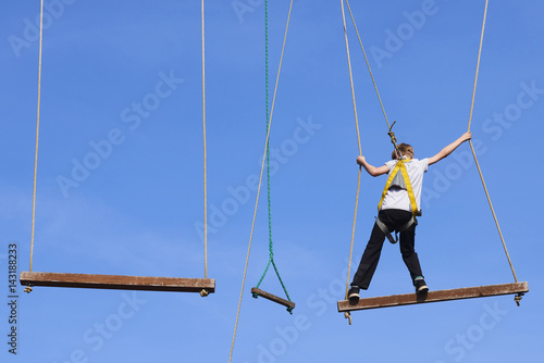 Cute school boy enjoying a sunny day in a climbing adventure activity park. Clear blue sky background. Children summer activities.