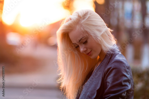 Beautiful young blonde girl with a pretty smiling face and beautiful eyes. A woman with long hair dispels their, amazing looks at sunset. Hot girl with a tender look, posing outdoor on city streets.