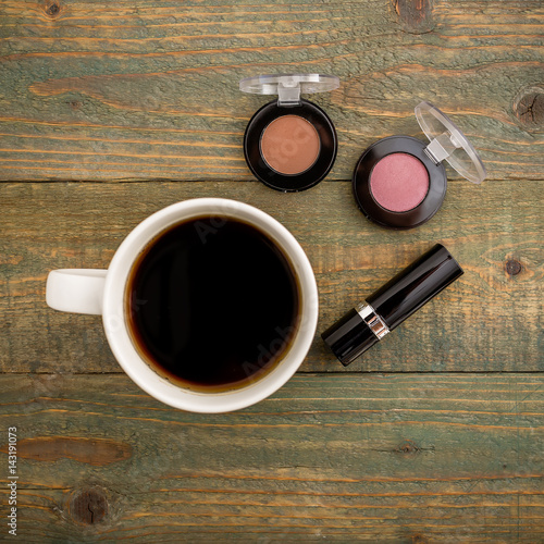 Feminine desk with cosmetics, lipstick and hot coffee on wooden background. Beauty background. Flat lay, top view