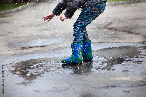 Boy in blue with green rubber boots jumped into deep puddle.