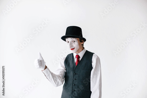 Mime in black hat and waistcoat holds his thumb up