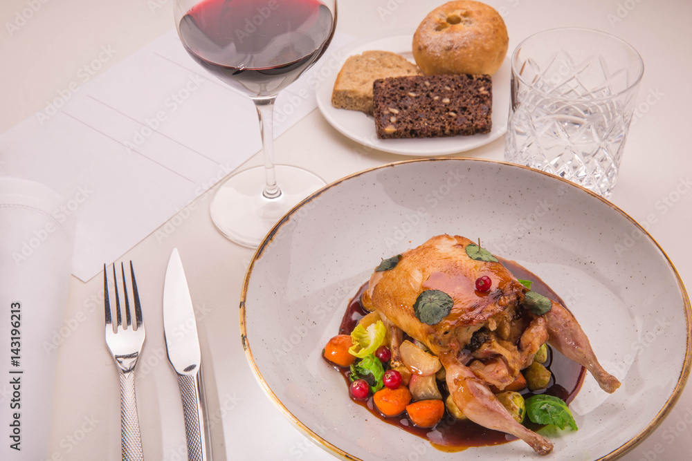 Table layout by the stuffed quail with sauce from a lavender, root crops and red currant with a glass of red wine and a basket of home-made bread